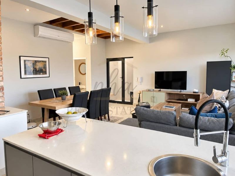 Modern open-plan living area featuring a sleek kitchen island with quartz countertops, contemporary pendant lighting, and exposed timber ceiling beams.