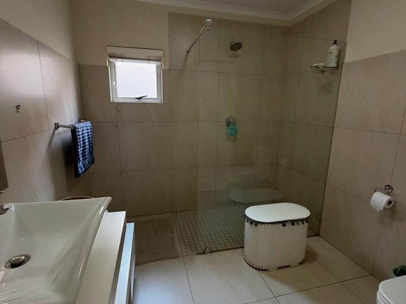 A functional bathroom featuring a walk-in shower with a glass screen, wall-mounted basin, and neutral floor-to-ceiling tiling.