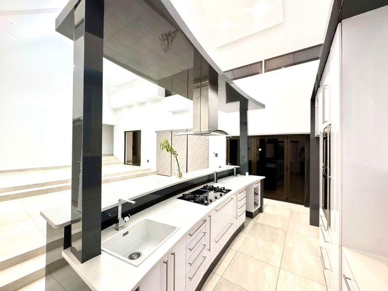 Modern, high-end kitchen featuring sleek white cabinetry, stone countertops, integrated gas hob, extractor fan, and premium tiled flooring in an open-plan layout.