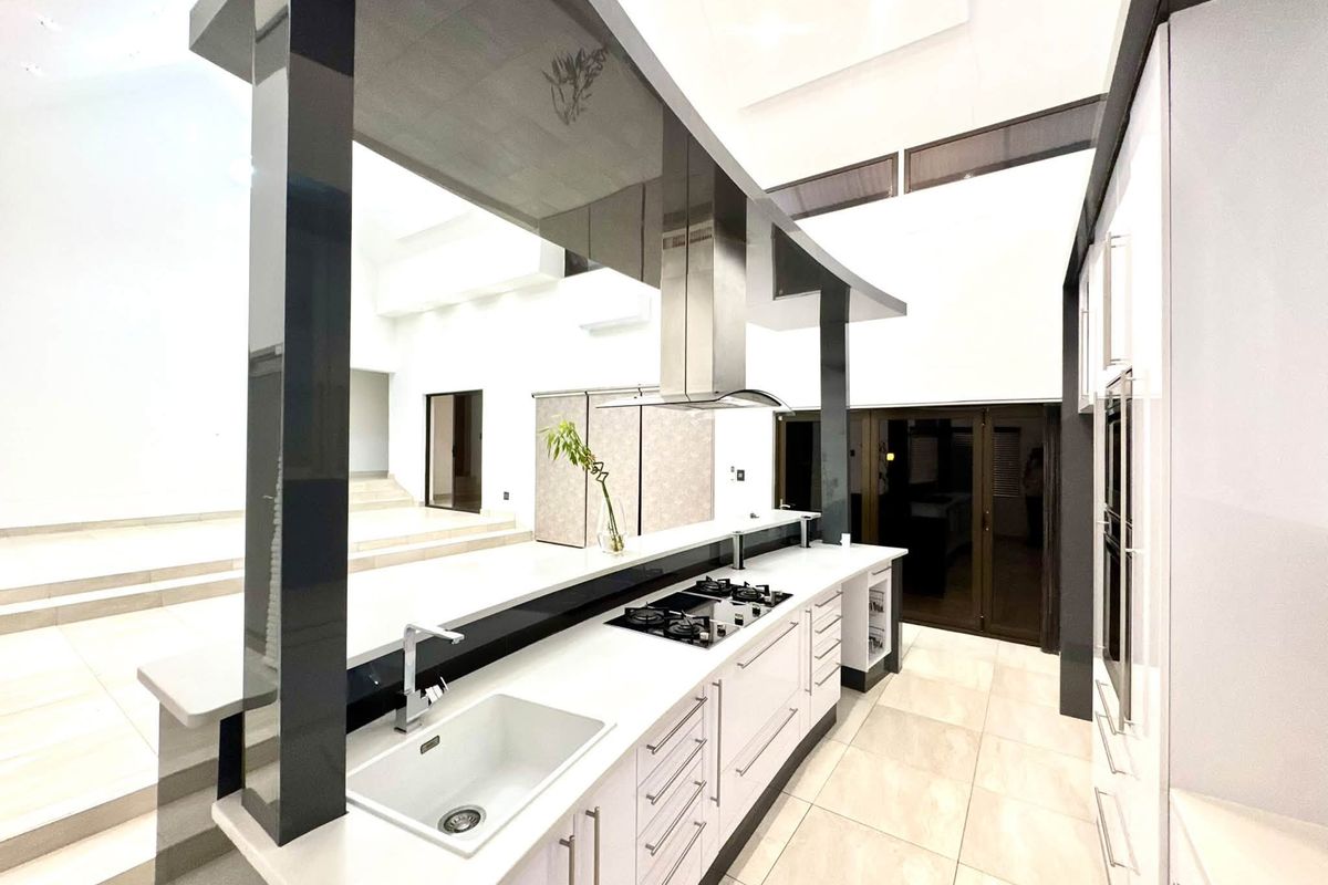 Modern, high-end kitchen featuring sleek white cabinetry, stone countertops, integrated gas hob, extractor fan, and premium tiled flooring in an open-plan layout.
