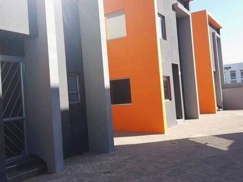 Modern industrial-style building exterior featuring a paved driveway, vibrant orange and grey facade, and secure entrance points.