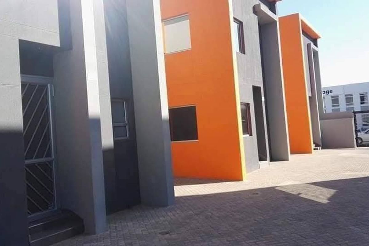 Modern industrial-style building exterior featuring a paved driveway, vibrant orange and grey facade, and secure entrance points.
