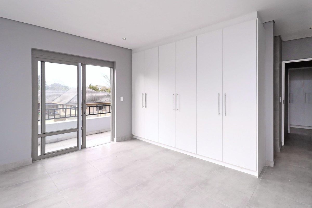 A bright, modern bedroom featuring neutral tiled flooring, extensive built-in cabinetry, and a sliding glass door leading to an outdoor balcony.