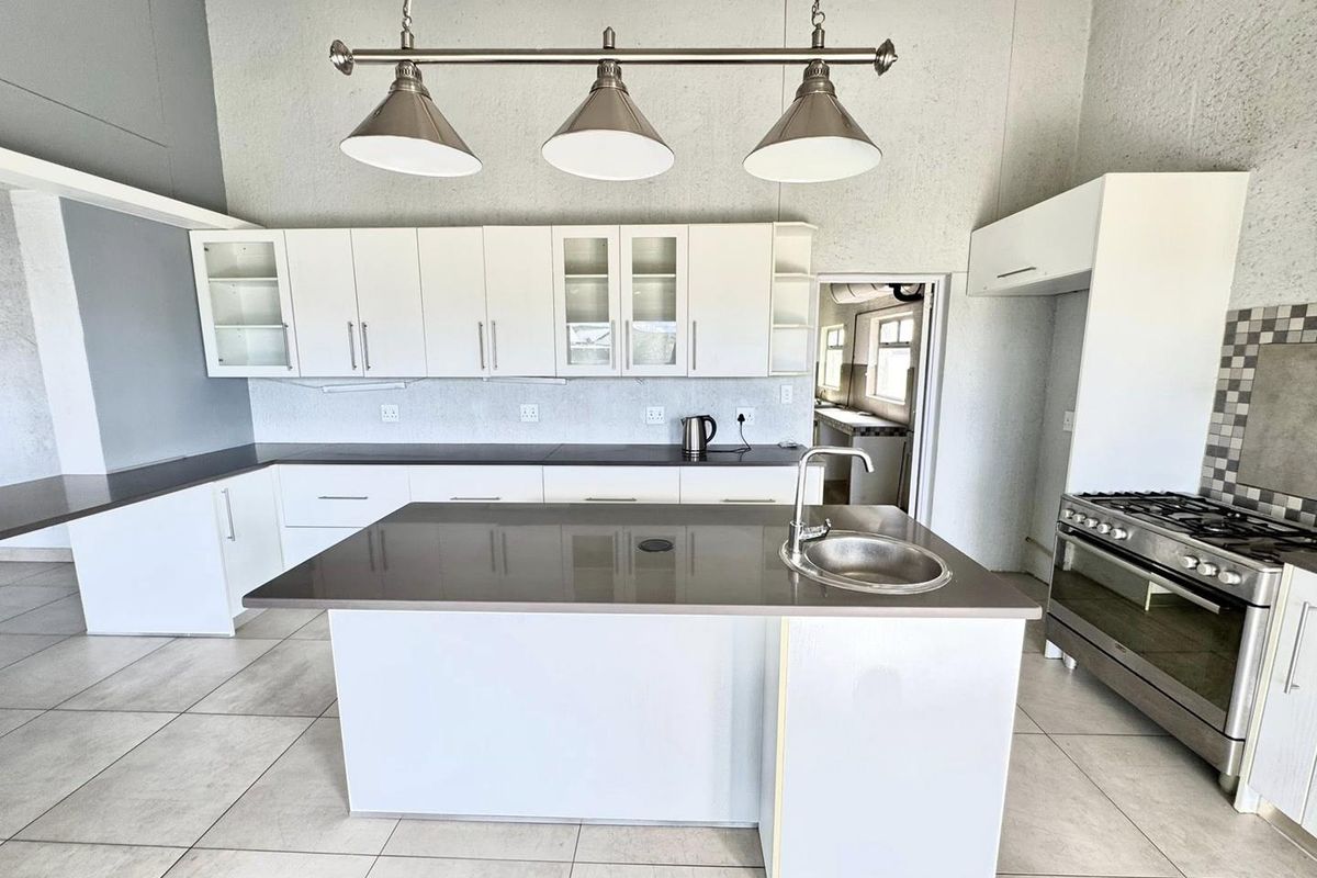 Modern kitchen featuring a central island with a prep sink, white cabinetry, stone countertops, and a stainless steel gas stove.