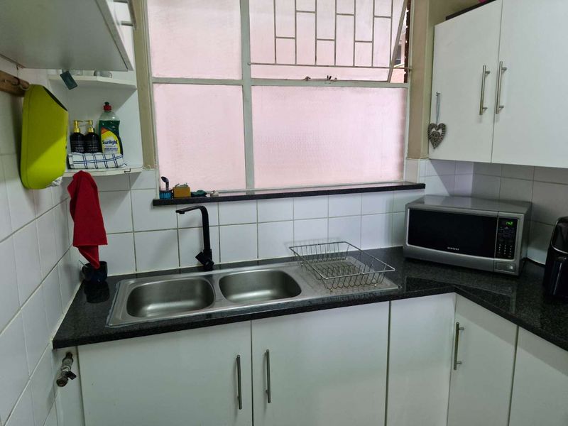 A functional kitchen area featuring white cabinetry, a dark granite countertop, a double stainless steel sink, and a window with security bars.