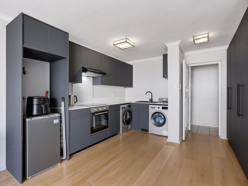 Modern kitchen featuring sleek dark grey cabinetry, stone countertops, integrated appliances, and light wood-look laminate flooring in an open-plan layout.