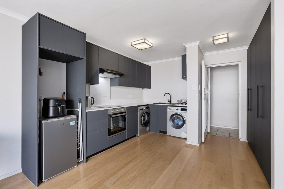Modern kitchen featuring sleek dark grey cabinetry, stone countertops, integrated appliances, and light wood-look laminate flooring in an open-plan layout.