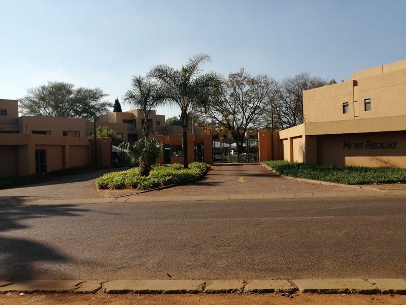The entrance to Mont Serrat apartment complex featuring a paved driveway, secure gated access, and established landscaped garden beds.