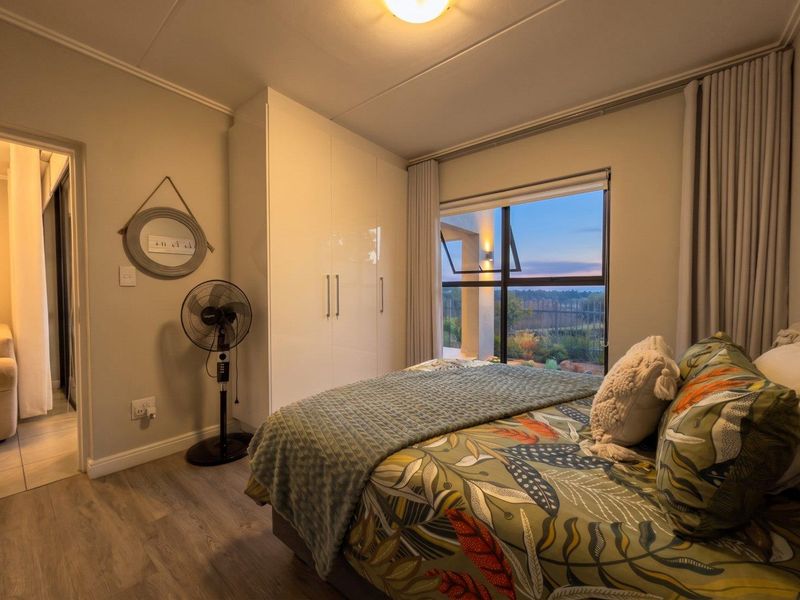 A well-maintained bedroom featuring built-in cupboards, modern laminate flooring, and a large window with views of the surrounding landscape.