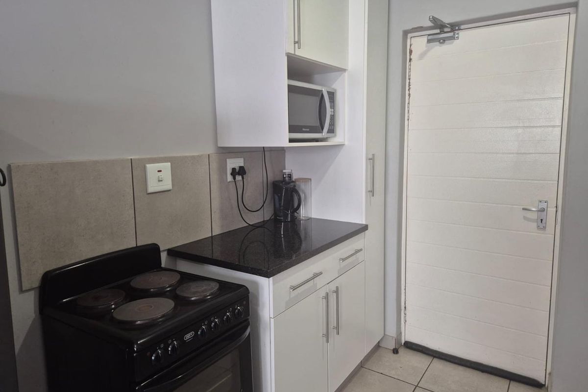 Compact kitchen area featuring built-in cabinetry, granite countertops, a freestanding electric stove, and a built-in microwave nook, adjacent to a secure entrance door.