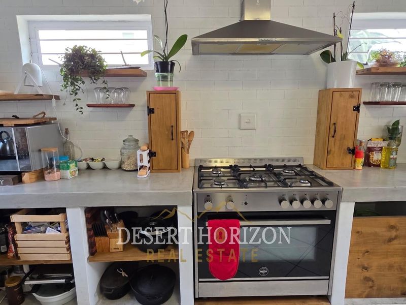 A rustic-style kitchen featuring a gas stove, stainless steel extractor fan, concrete countertops, and open shelving against a white brick splashback.
