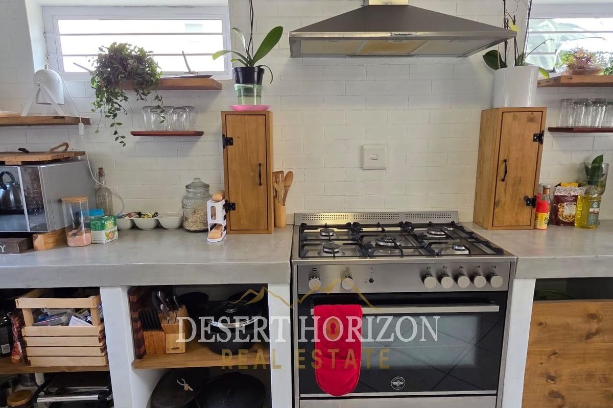 A rustic-style kitchen featuring a gas stove, stainless steel extractor fan, concrete countertops, and open shelving against a white brick splashback.