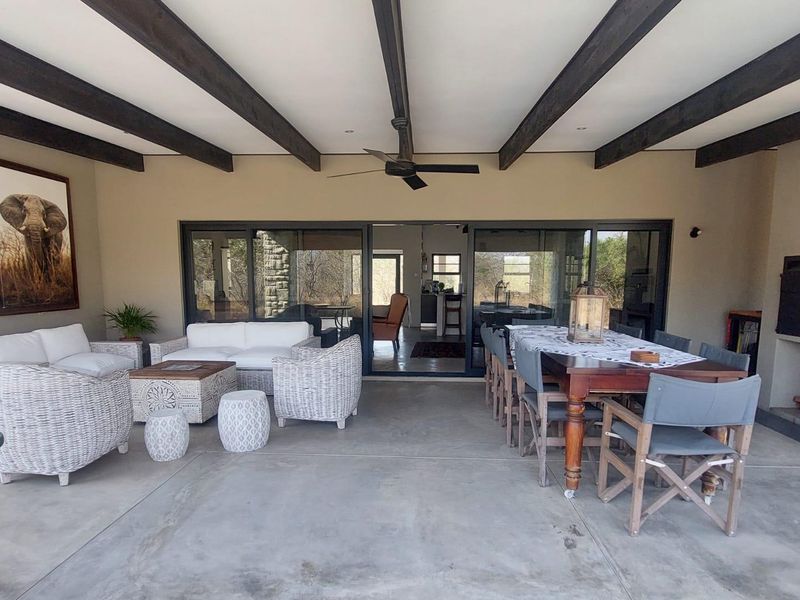 Spacious covered patio featuring exposed timber beams, a ceiling fan, concrete flooring, and a built-in fireplace, seamlessly connecting to the interior living space.