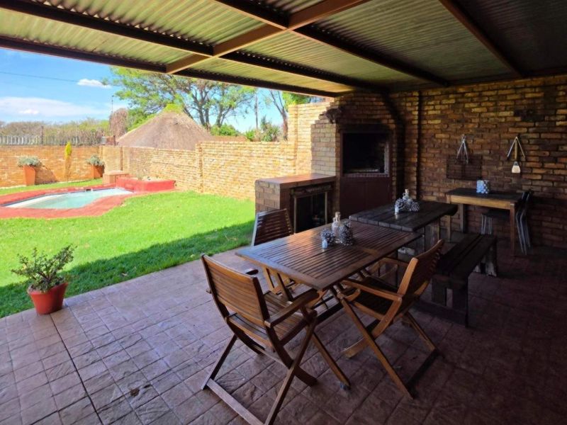 Covered outdoor patio featuring a built-in braai, tiled flooring, and direct access to the garden and swimming pool area.