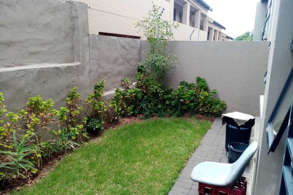 A compact rear garden area featuring a small lawn, paved walkway, and high boundary walls with integrated electric fencing.