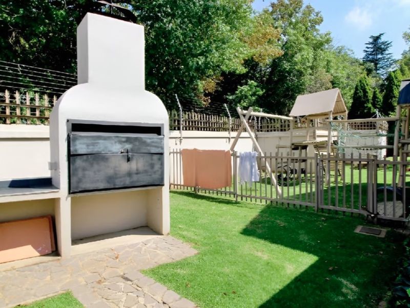 A private garden area featuring a built-in braai, stone paving, and secure perimeter fencing with electric security wires.