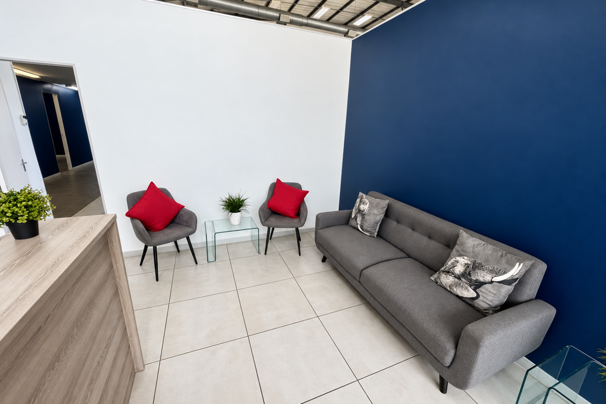 A modern reception or waiting area featuring tiled flooring, an exposed industrial ceiling, and a bold blue accent wall.
