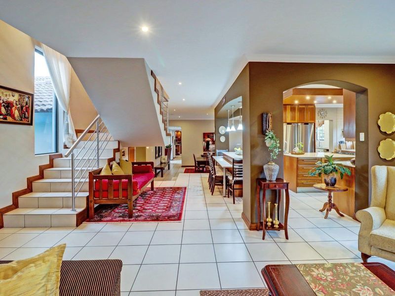 Spacious open-plan living area featuring tiled floors, a modern staircase with stainless steel railings, and a seamless transition into the kitchen space.