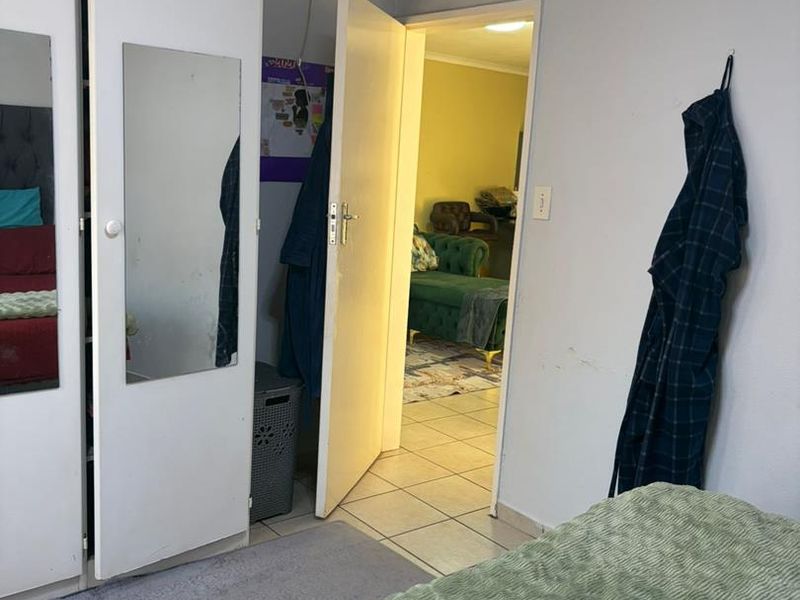A bedroom featuring built-in wardrobes and tiled flooring, with a view through the doorway into an adjacent living space.