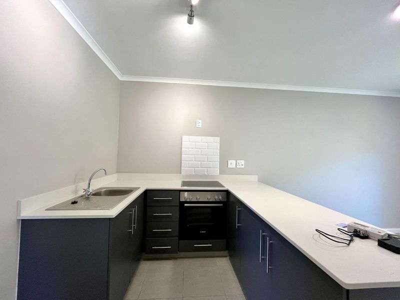 Modern kitchen featuring dark cabinetry, white quartz countertops, a built-in oven, electric hob, and a stainless steel sink with subway tile splashback.