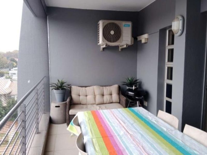 A covered balcony featuring a metal balustrade, wall-mounted lighting, and an external air conditioning unit.