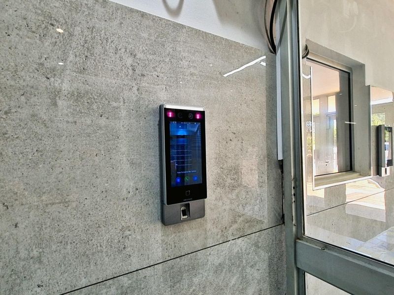 Modern building entrance featuring a high-tech biometric access control system mounted on polished stone wall cladding with glass door access.