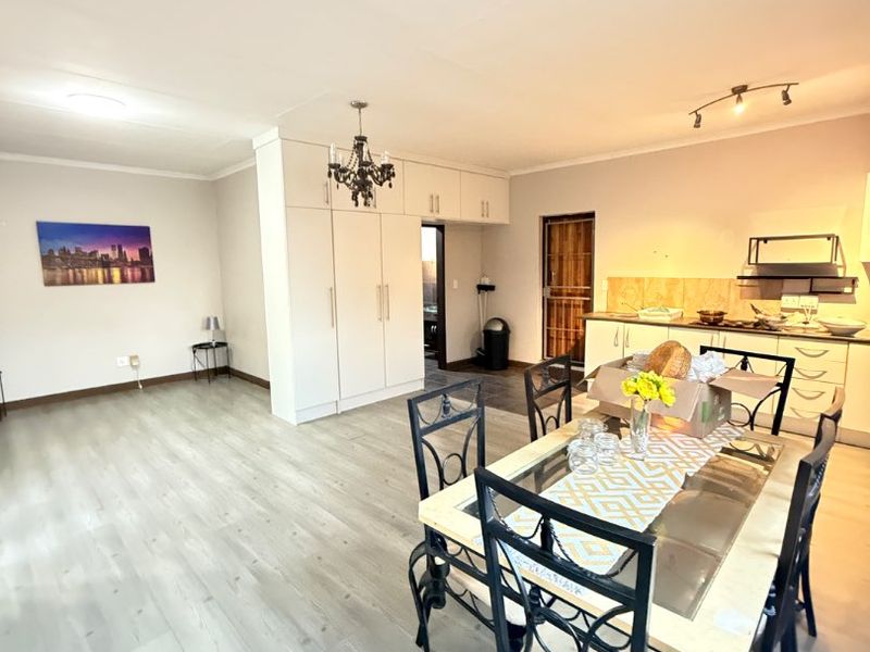 Open-plan living and dining area featuring light laminate flooring, built-in kitchen cabinetry, and an integrated extractor fan in a bright, functional layout.