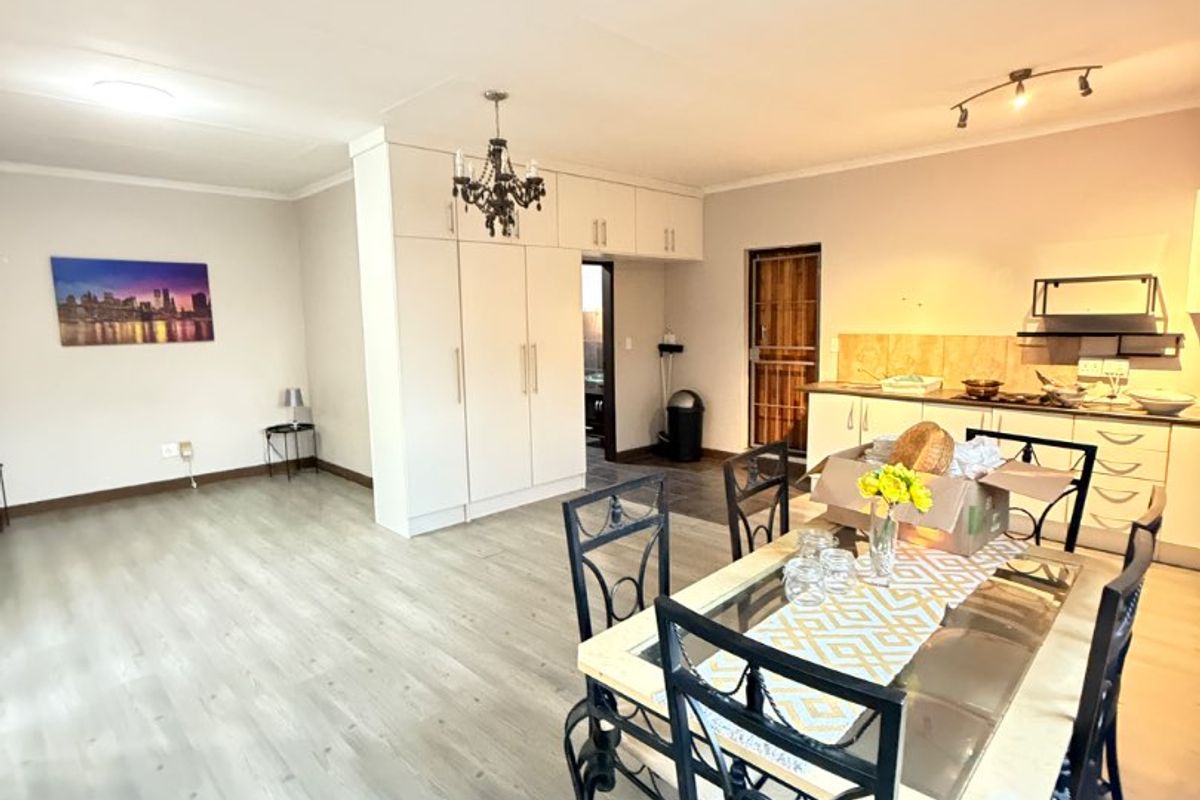 Open-plan living and dining area featuring light laminate flooring, built-in kitchen cabinetry, and an integrated extractor fan in a bright, functional layout.