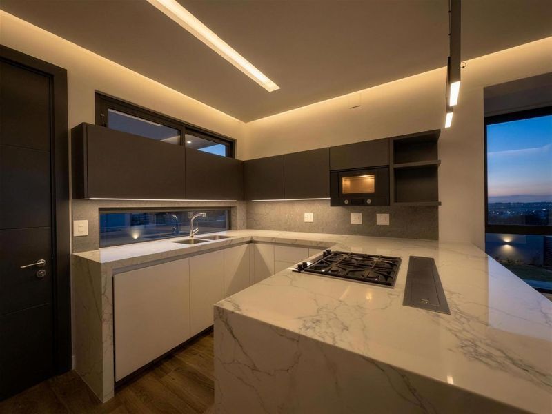 Modern kitchen featuring a marble waterfall island, gas hob, integrated appliances, and sleek handleless cabinetry with ambient LED strip lighting.