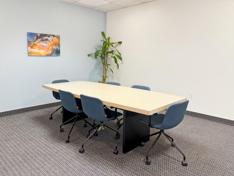 A functional office meeting room featuring neutral walls, carpeted flooring, and a suspended ceiling, suitable for professional use.