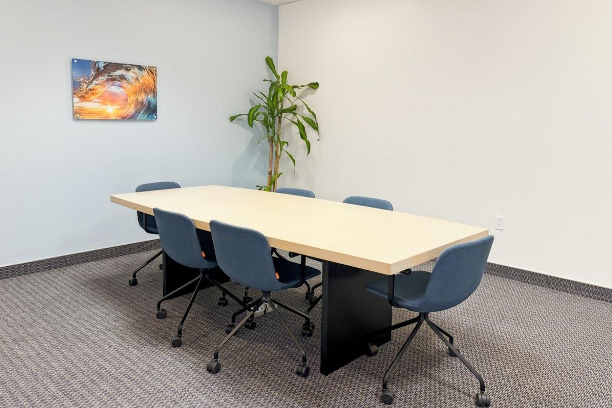 A functional office meeting room featuring neutral walls, carpeted flooring, and a suspended ceiling, suitable for professional use.
