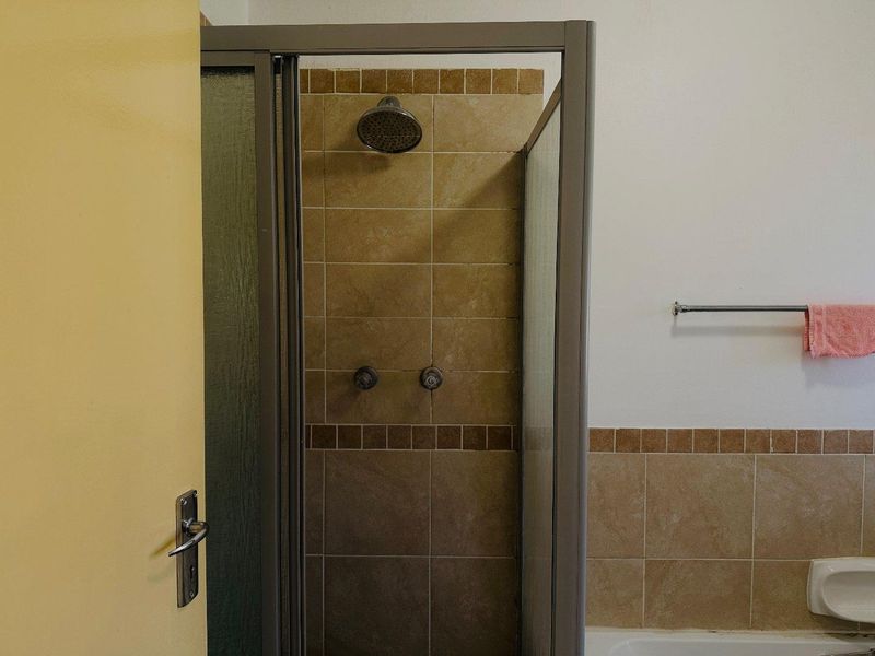 A functional bathroom featuring a tiled shower enclosure with a fixed shower head and a wall-mounted towel rail.