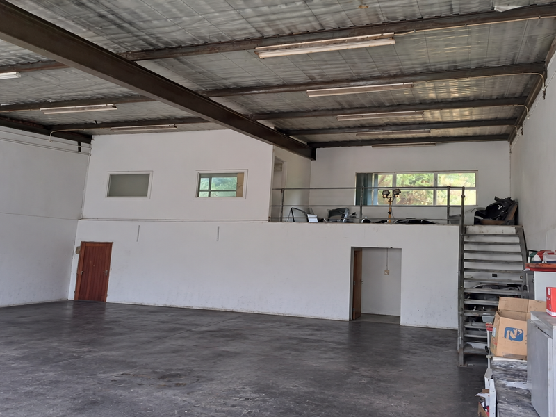 Spacious industrial warehouse unit featuring high ceilings with exposed steel beams, a mezzanine level with metal staircase, and durable concrete flooring.