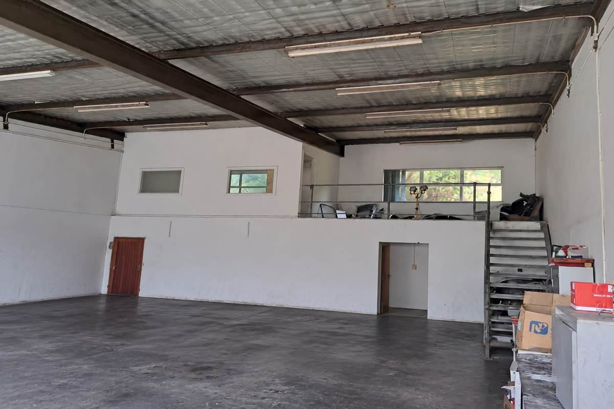 Spacious industrial warehouse unit featuring high ceilings with exposed steel beams, a mezzanine level with metal staircase, and durable concrete flooring.