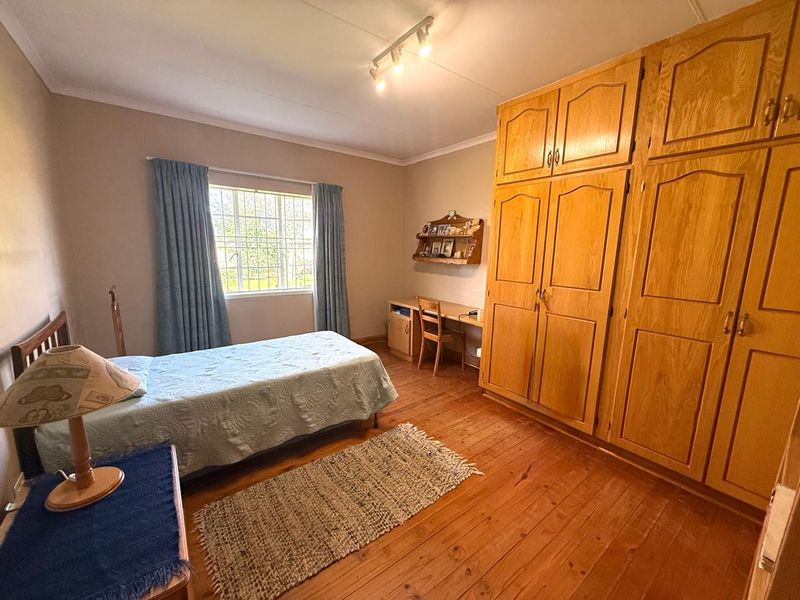 A bedroom featuring warm wooden flooring, extensive built-in wooden cabinetry, and a window with security bars, offering a functional and traditional living space.