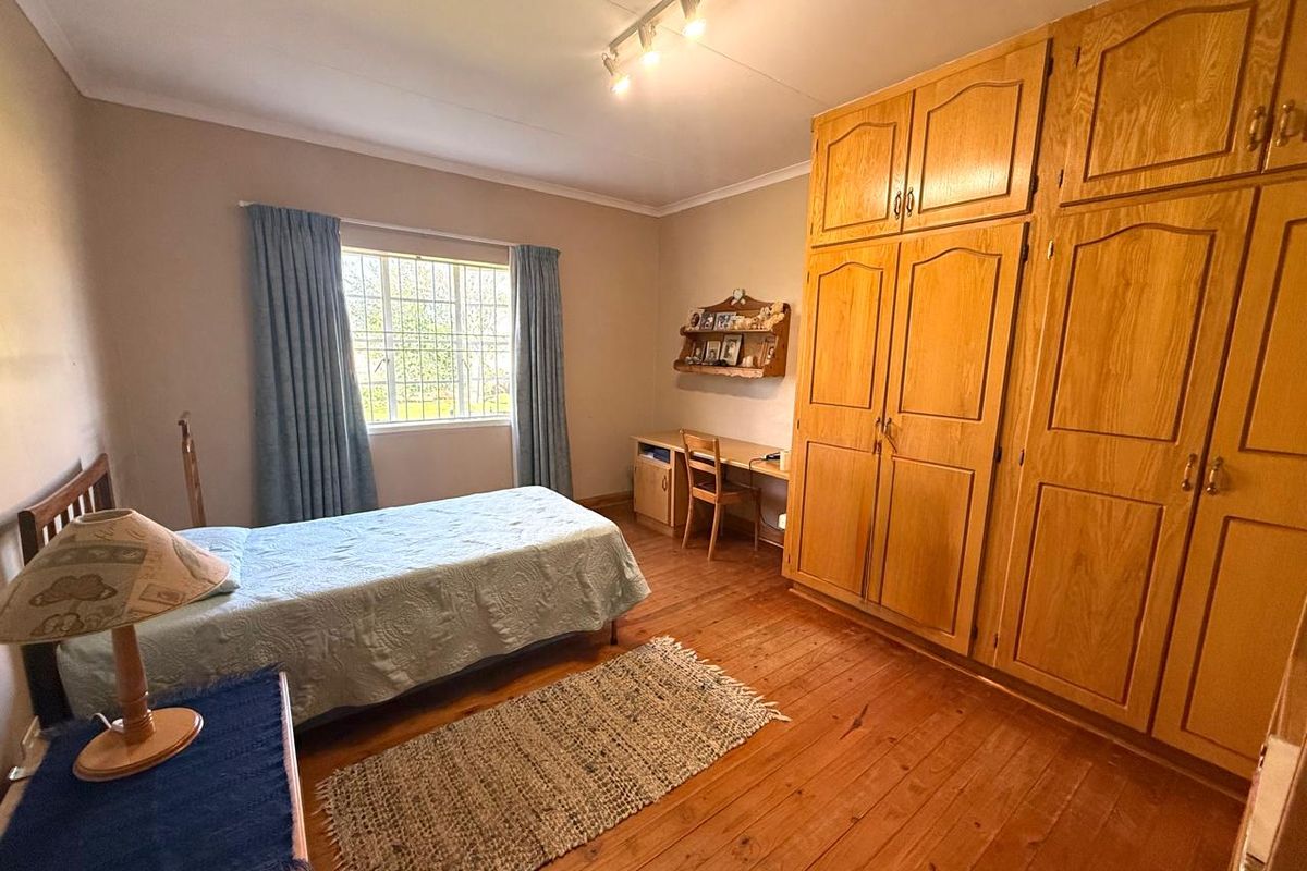 A bedroom featuring warm wooden flooring, extensive built-in wooden cabinetry, and a window with security bars, offering a functional and traditional living space.