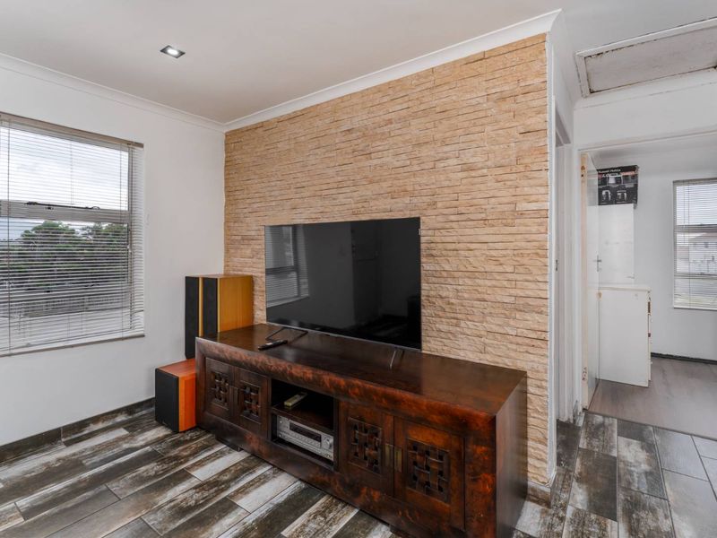 Living room featuring a textured stone feature wall, tiled flooring, and recessed lighting, with an adjacent hallway leading to a secondary space.