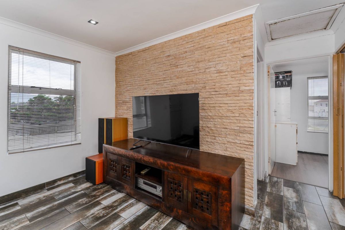 Living room featuring a textured stone feature wall, tiled flooring, and recessed lighting, with an adjacent hallway leading to a secondary space.