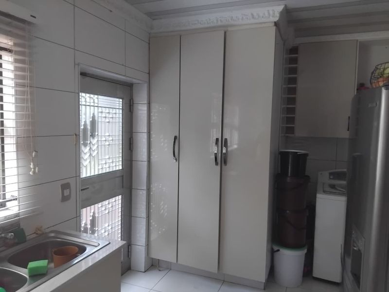 A functional laundry area featuring built-in cabinetry, tiled finishes, and a stainless steel sink with direct access to the exterior.