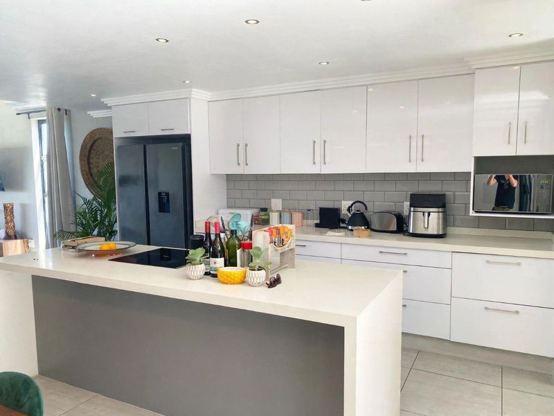 Modern kitchen featuring a large central island, sleek white cabinetry, quartz countertops, subway tile backsplash, and integrated appliances.