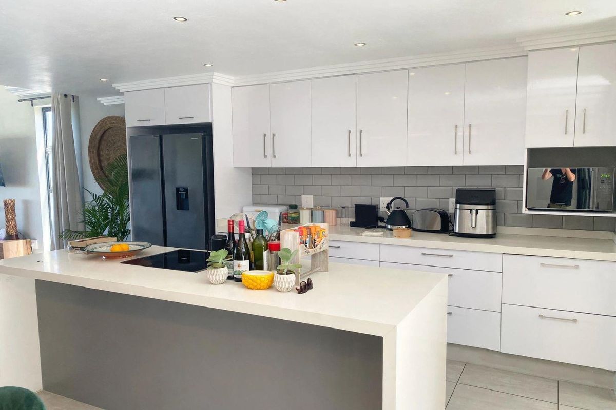 Modern kitchen featuring a large central island, sleek white cabinetry, quartz countertops, subway tile backsplash, and integrated appliances.