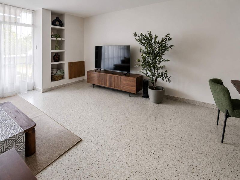 A bright and modern living room featuring high-quality terrazzo flooring, built-in wall shelving, and a sliding glass door providing natural light.