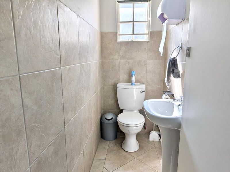 A compact office bathroom featuring a pedestal sink, toilet, and neutral ceramic wall and floor tiling.