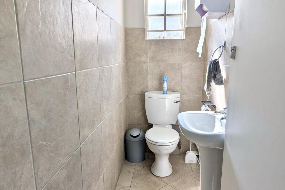 A compact office bathroom featuring a pedestal sink, toilet, and neutral ceramic wall and floor tiling.