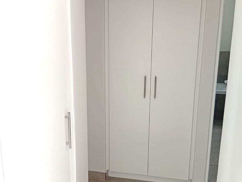 A clean, minimalist hallway featuring built-in white cupboards and neutral tiled flooring, providing efficient storage and a seamless transition between rooms.