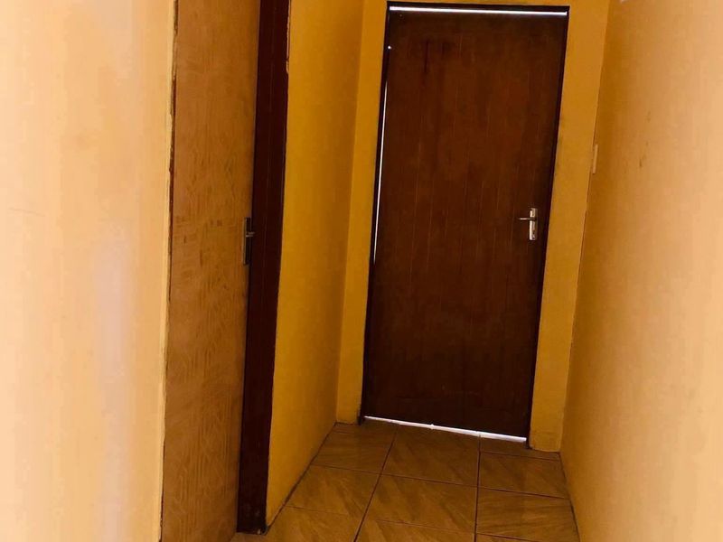 A narrow interior hallway featuring tiled flooring and two wooden internal doors, requiring cosmetic updates to the wall finishes.