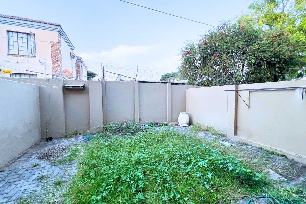 A private rear courtyard area featuring high boundary walls with security fencing and a small paved section with overgrown lawn.