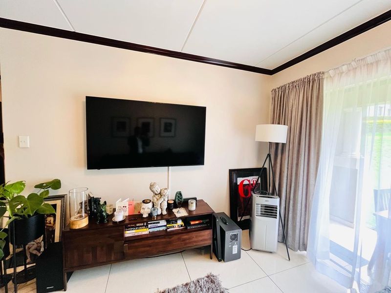 A bright living room featuring tiled flooring, neutral walls with dark ceiling trim, and a sliding glass door providing access to the outdoors.