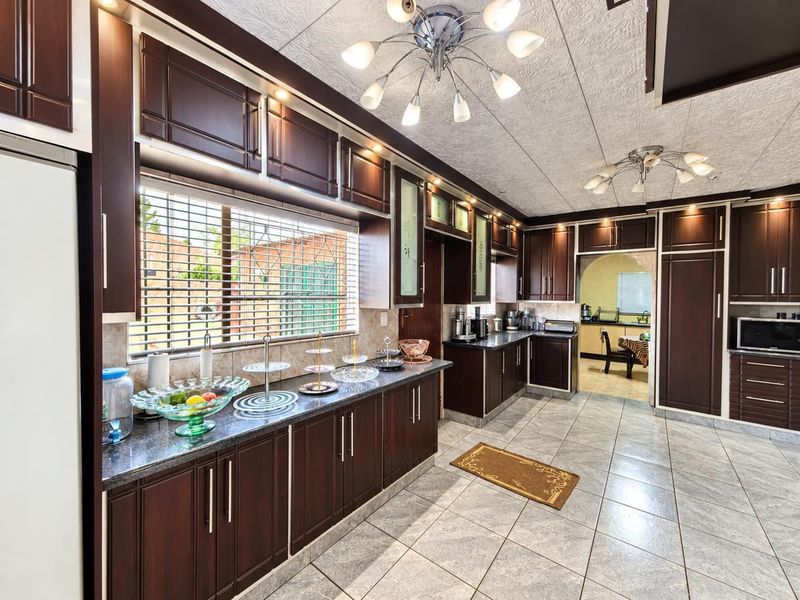 Spacious kitchen featuring dark wood cabinetry, granite countertops, tiled flooring, and integrated appliances, with an adjacent scullery area visible through the archway.