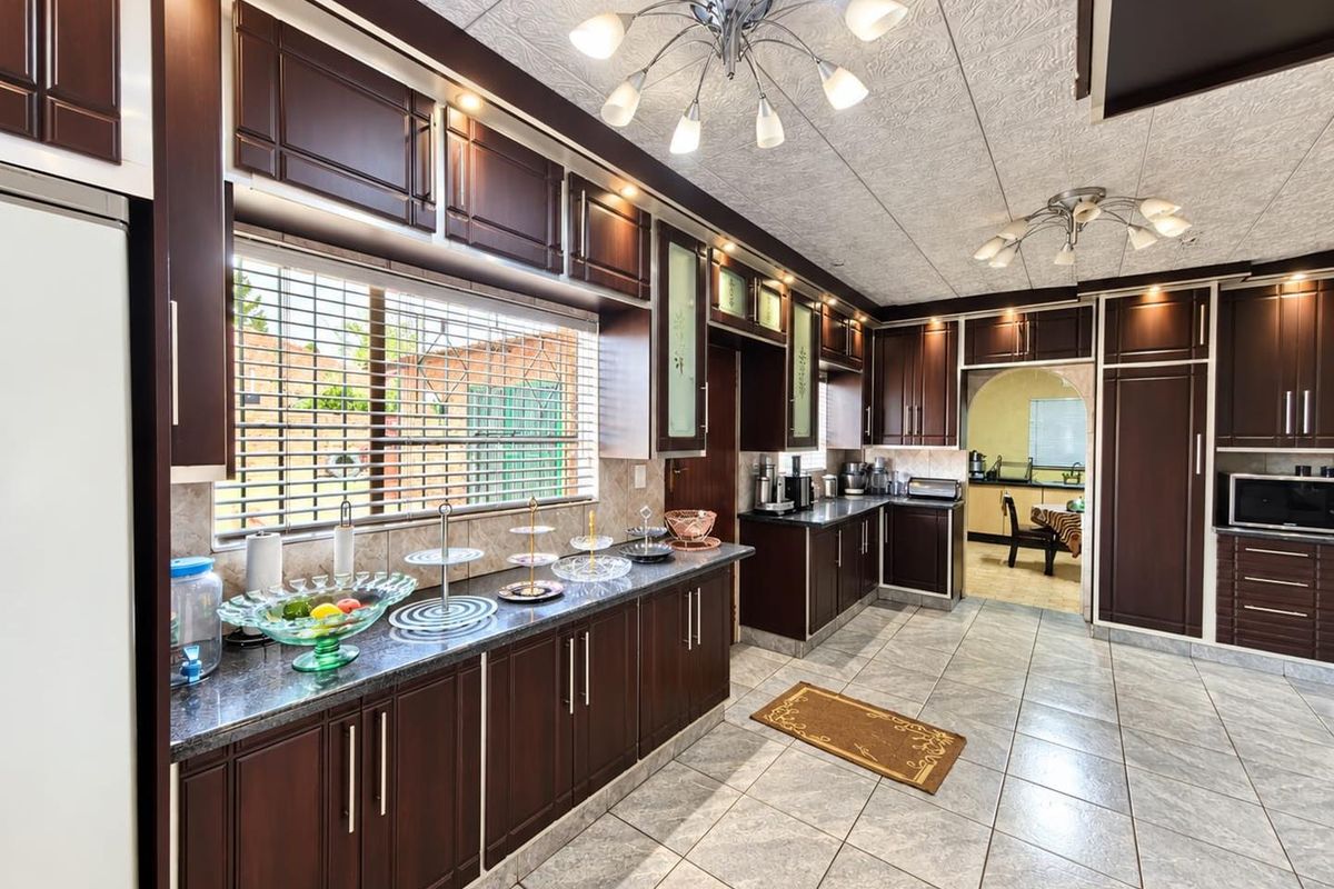 Spacious kitchen featuring dark wood cabinetry, granite countertops, tiled flooring, and integrated appliances, with an adjacent scullery area visible through the archway.